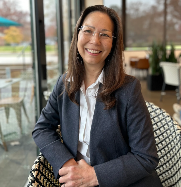 Image of woman with shoulder length long hair and glasses in a grey jacket smiling into the camera